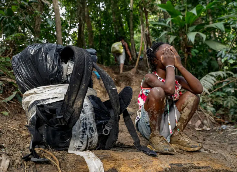 A girl covers her face. She is trying to cross the Darien Gap with her family. She has mud on her clothes and boots. Photo by Manuel Saldarriaga