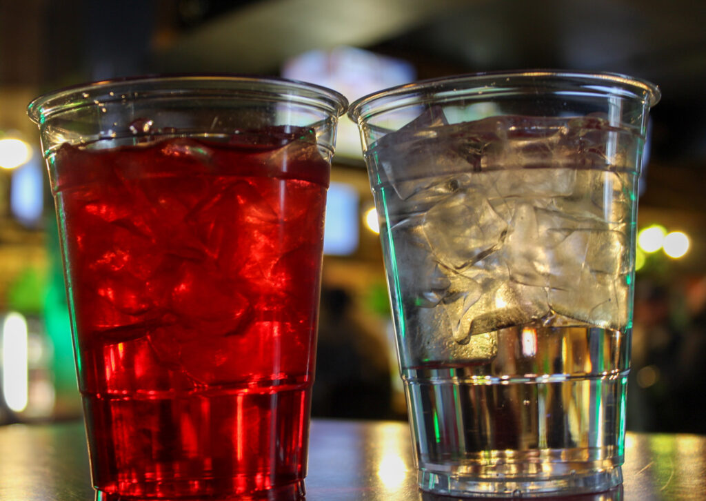 Two glasses with ice. One has water, the other one has cranberry juice. 