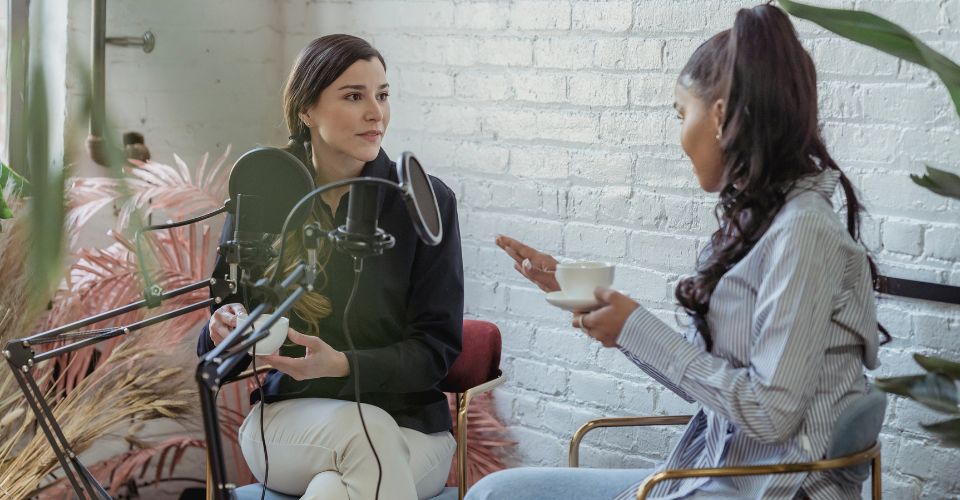 Two journalists talk in front of a microphone. Photo: Canva